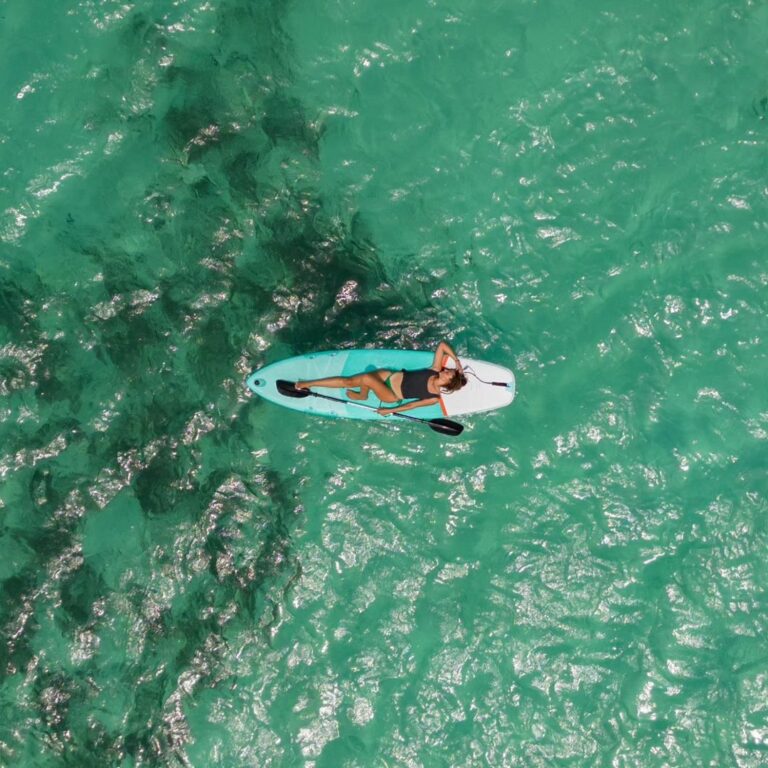 Woman paddleboarding over shallow coral reef in clear turquoise waters near San Blas