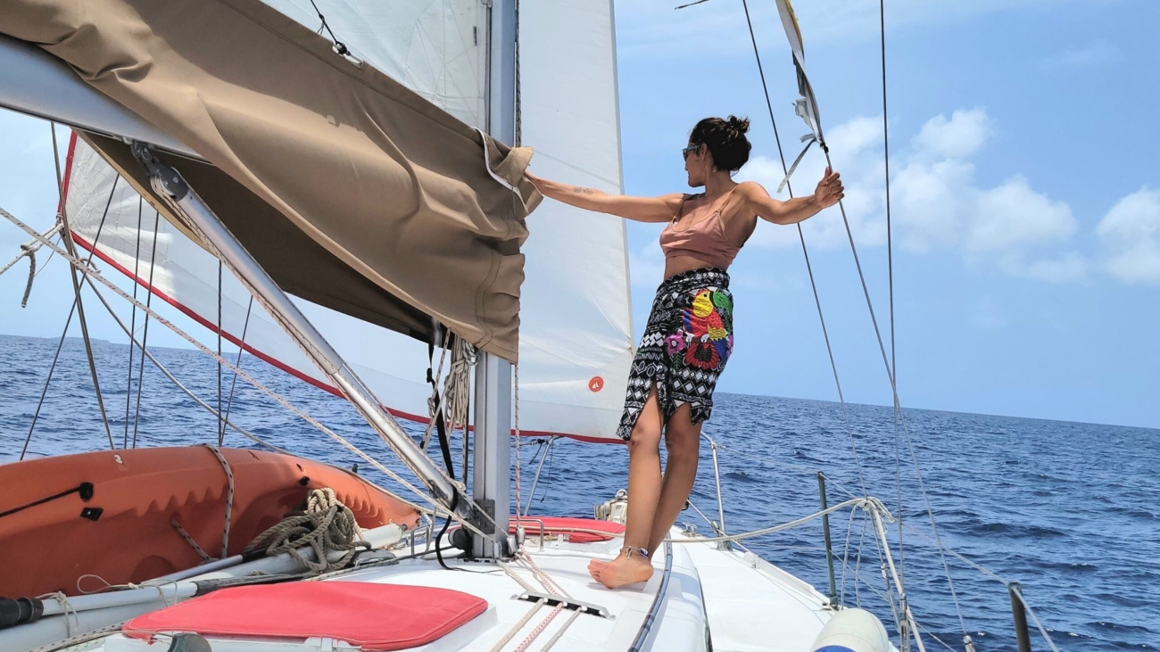 Woman sailing on a boat in San Blas, holding the mast and gazing at the horizon under a clear blue sky