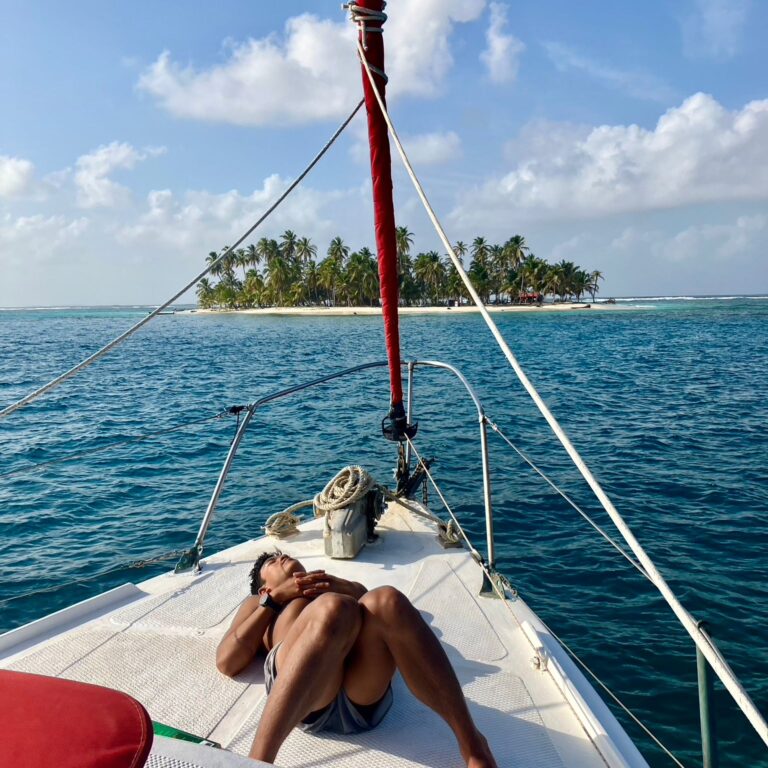 Traveler resting at the bow of a sailing boat facing a tropical island