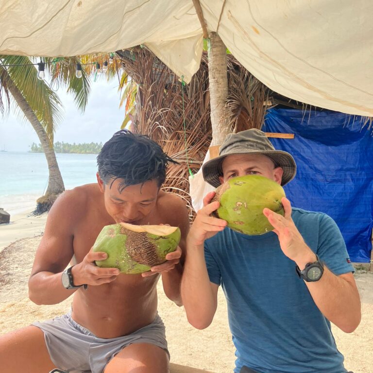 Two travelers drinking fresh coconuts on a palm-lined beach in Panama