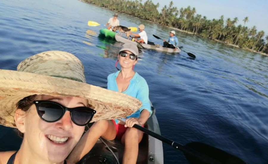 Group kayaking adventure in San Blas with smiling tourists paddling near a tropical shoreline