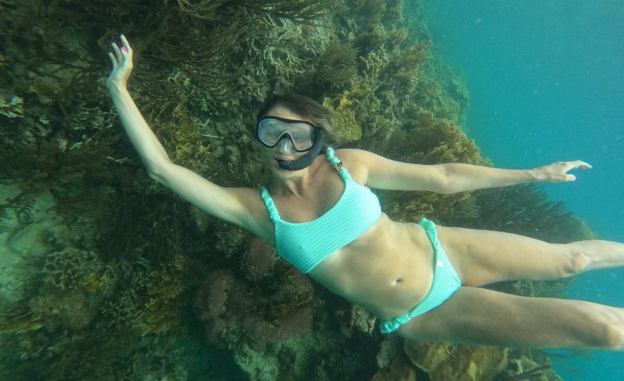 Woman snorkeling over colorful coral reef in warm, shallow Caribbean water