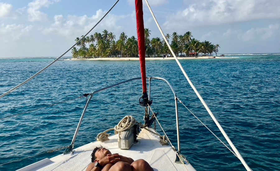 Traveler resting at the bow of a sailing boat facing a tropical island