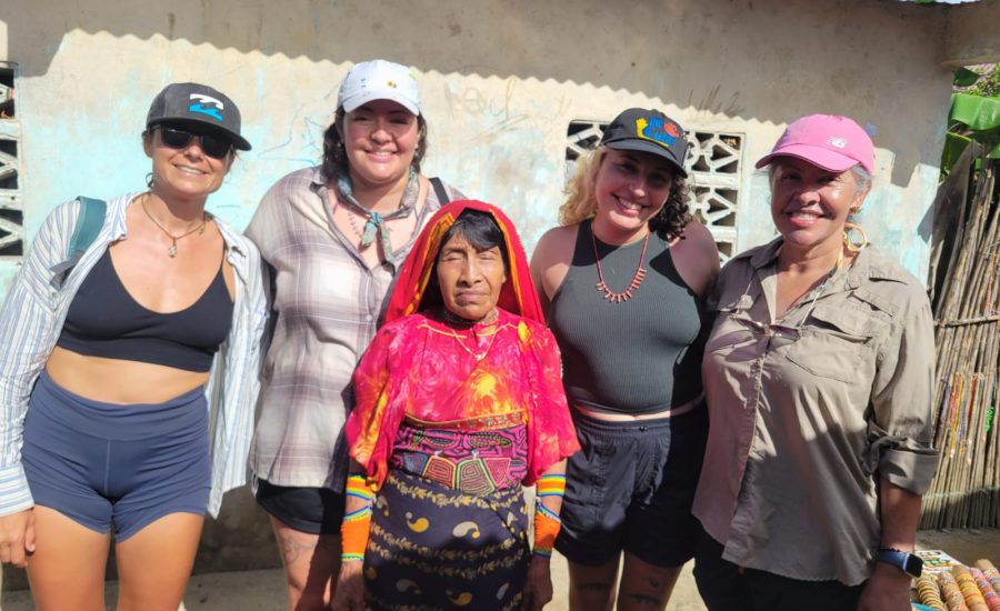 Travelers posing with a Guna family outside a thatched-roof home in San Blas